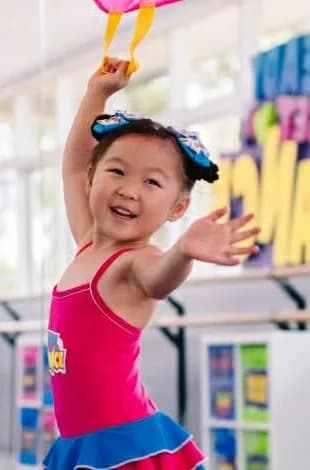 A little girl in a pink leotard dancing with a big smile